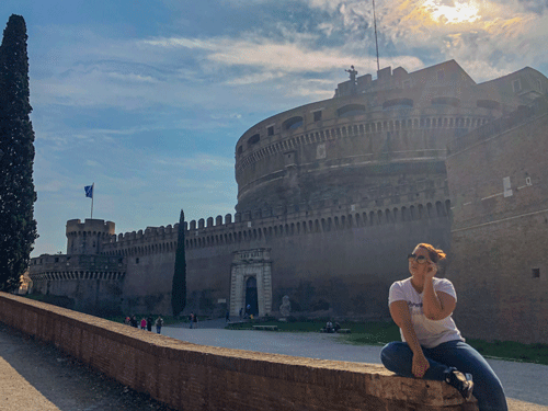 Castelo Sant'Angelo de fundo e Erika sentada na mureta do castelo