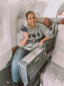 O que fazer em Roma: Poltrona da classe executiva do avião da Latam. Estou sentada segurando meu passaporte.